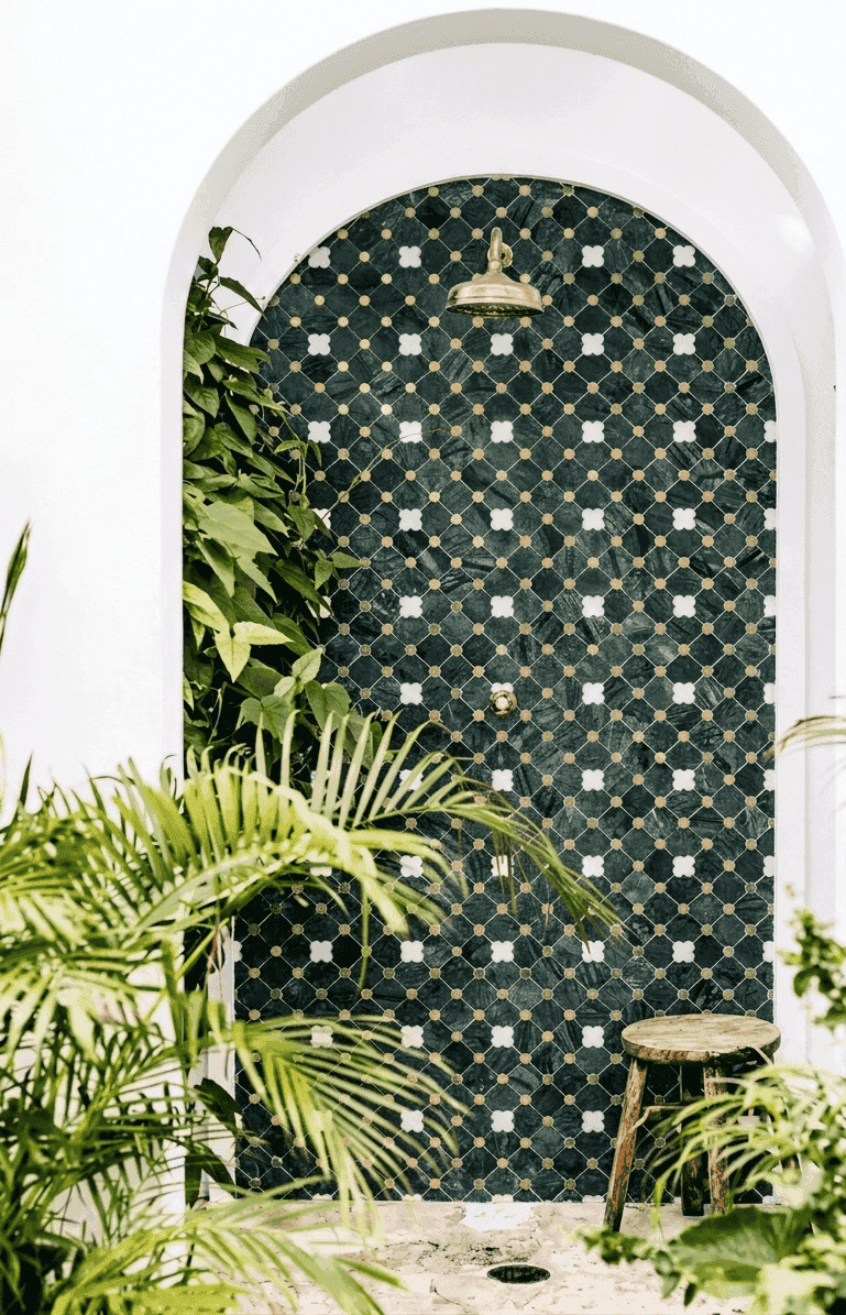 Ducha exterior con malla decorativa verde, detalles dorados y entorno tropical — showroom A.MODO